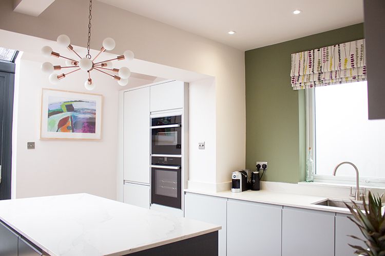 A wide shot of the kitchen area with the green wall and colourful blind.