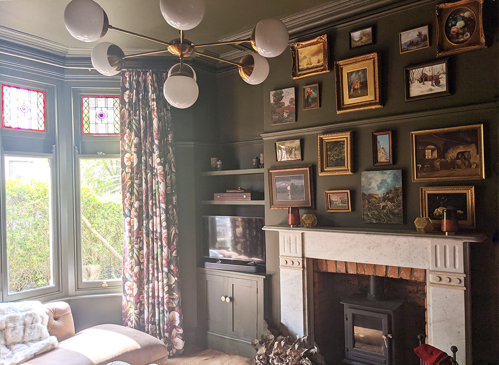 A photo of a dark green living room with gold accents in the lighting and picture frames.