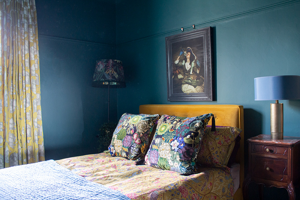 A photo of the middle bedroom of the house, painted in a rich teal colour with a mustard yellow velvet bed.