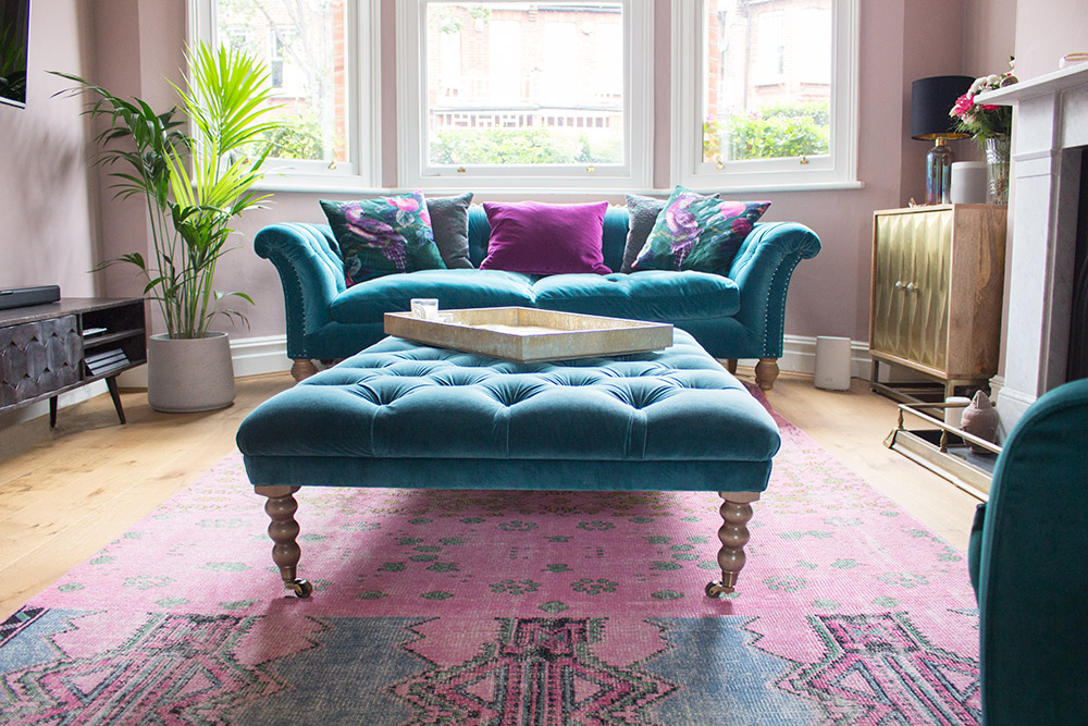 A photo of a teal sofa and footstool in a pink living room.