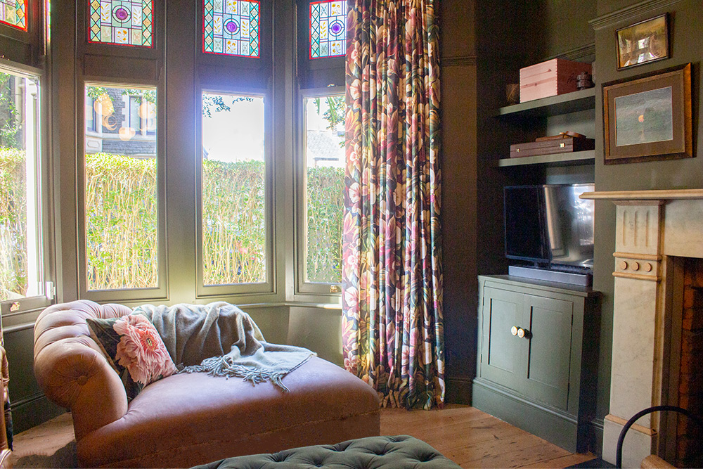 A living room project of ours with dark green walls and a leather chaise in the bay window.