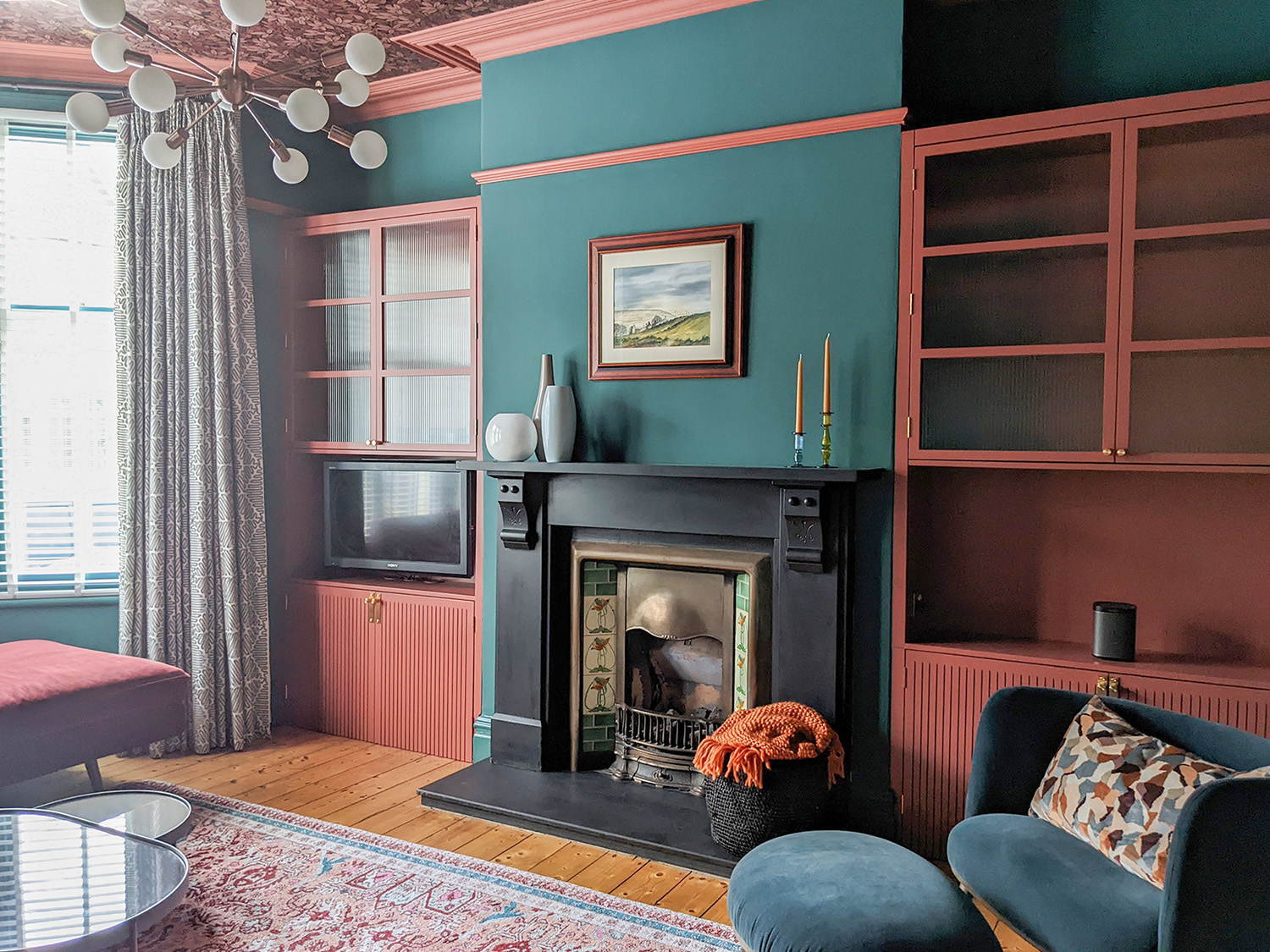A photo showing the living room with dark teal walls and light red built in cabinets.
