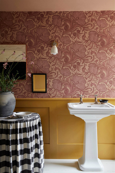 A photo of the Poppy Trial wallpaper in the Masquerade colourway, with yellow paneling and a white sink.