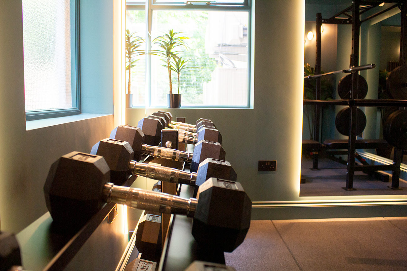 A photo taken along a row of weights in the finished gym, showing the lighting around the mirrors.
