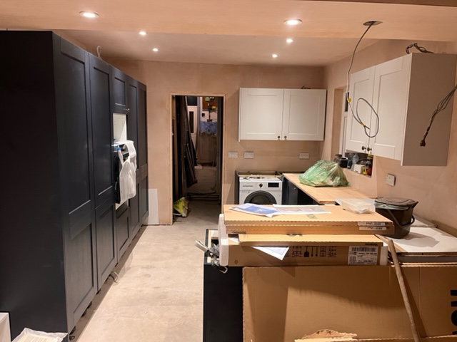 A kitchen with plastered walls and floor to ceiling navy cupboards 