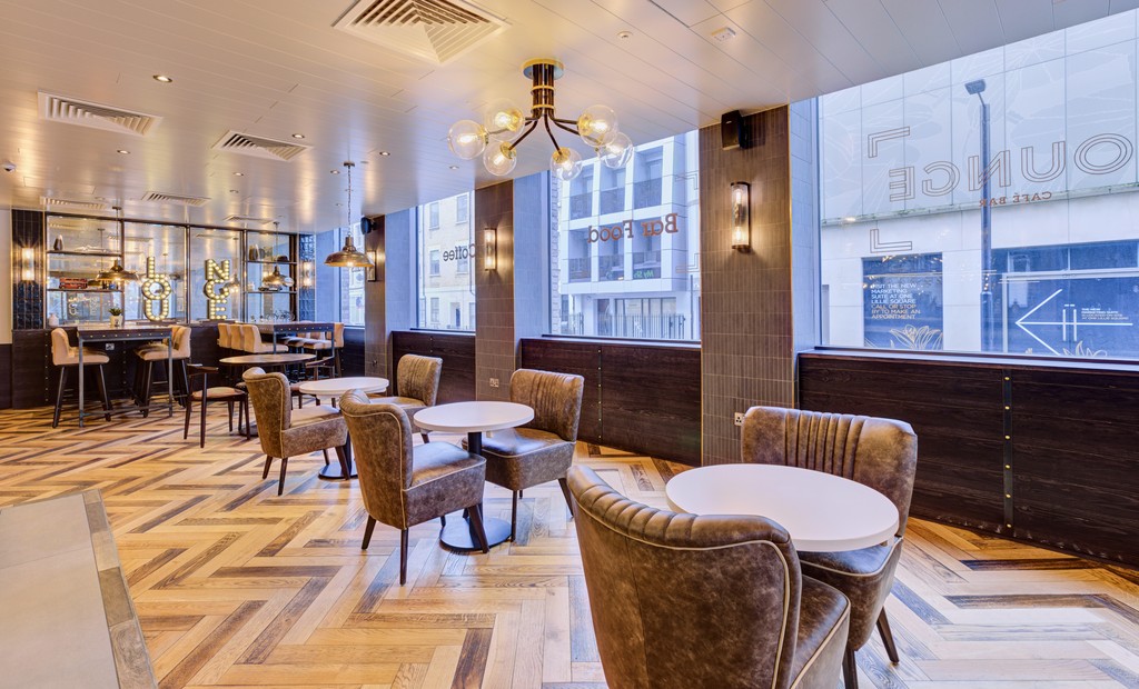 A bar seating area with wooden floors, round tables and large windows 