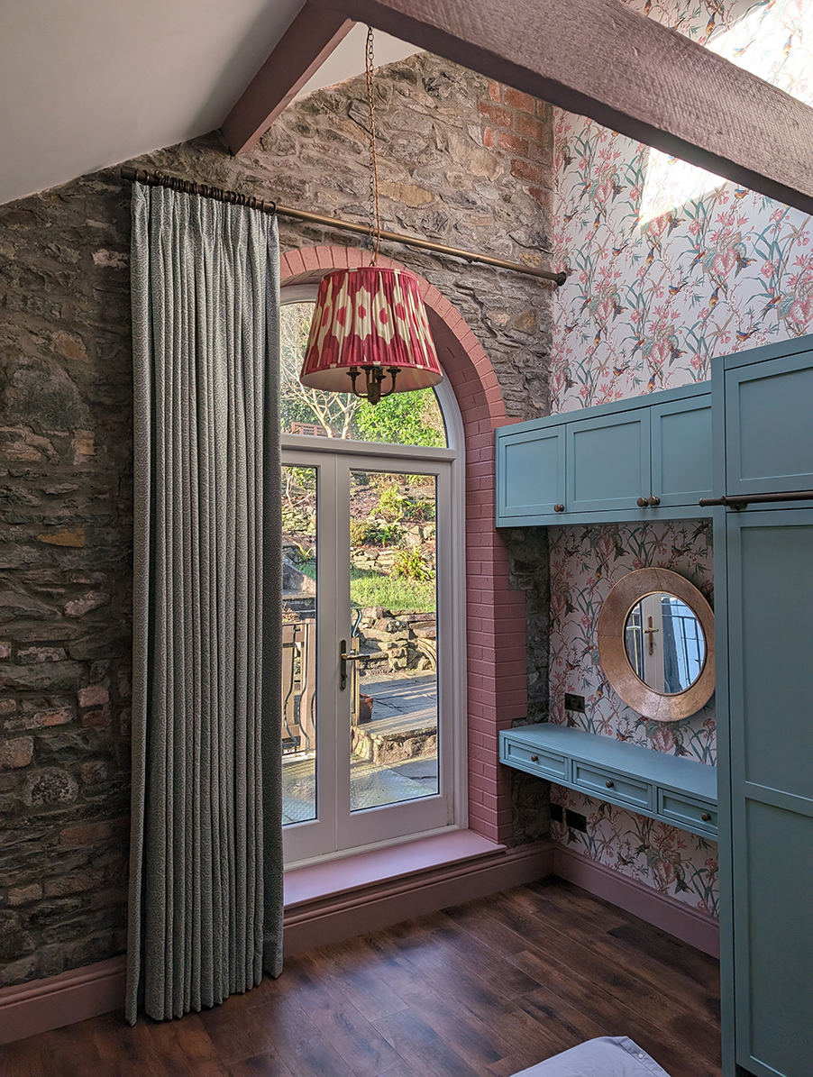 a bedroom with built in dressing table, blue curtains and pink ceiling lampshade