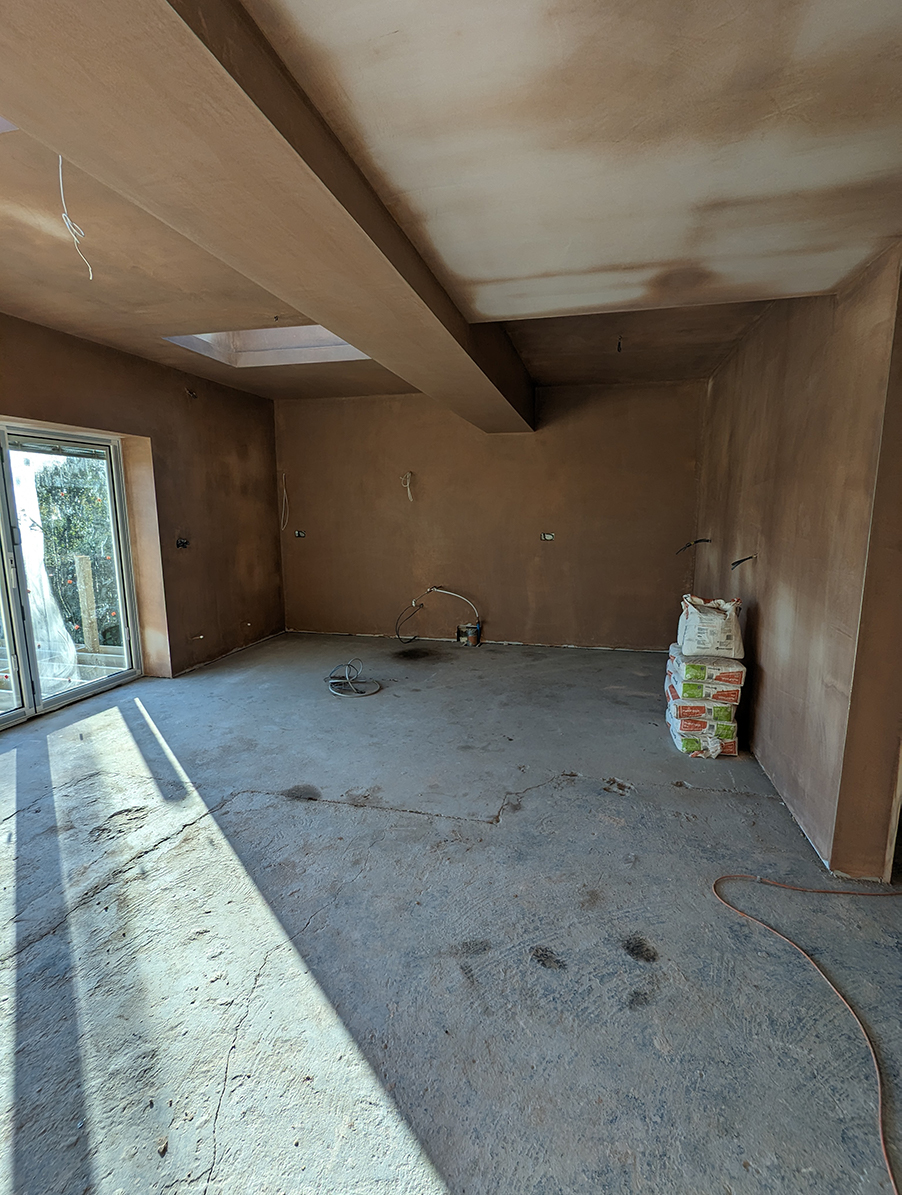 A room with bare plaster walls, a concrete floor and large bi fold doors 