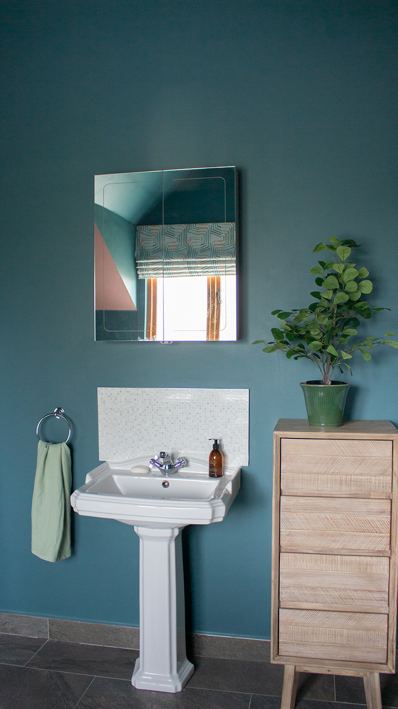 A photograph of a bathroom with teal walls and a white sink