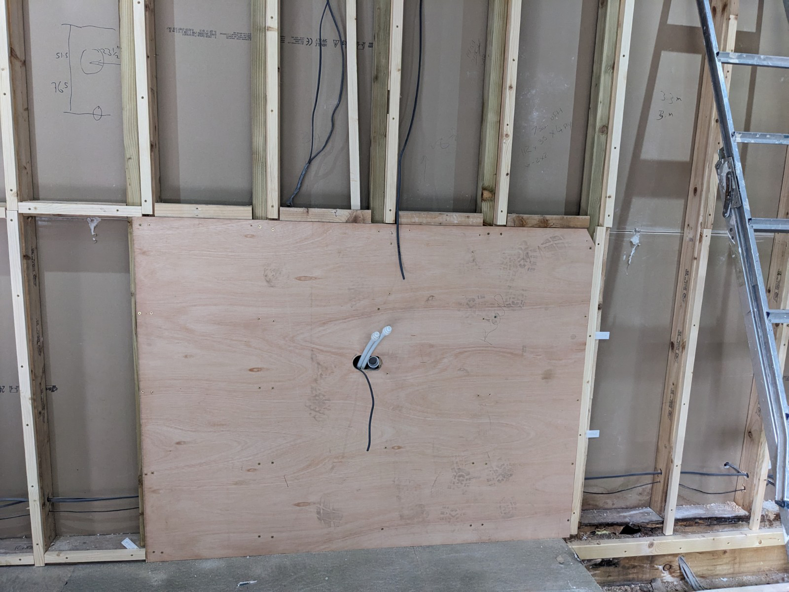 A photograph of a plywood board on a wall with pipework coming out