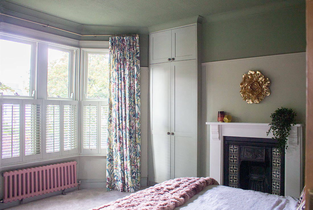 A photo of a main bedroom with patterned curtains hung at the bay window.