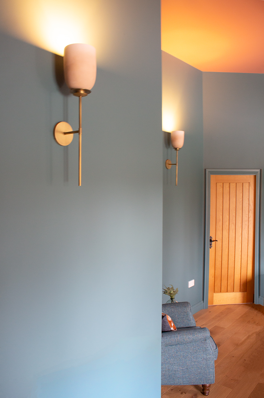 A photo of a teal painted bedroom with two pink wall lights washing the wall with a gentle glow of light.