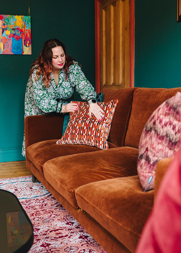 A photo of Louise plumping a cushion on a velvet sofa.