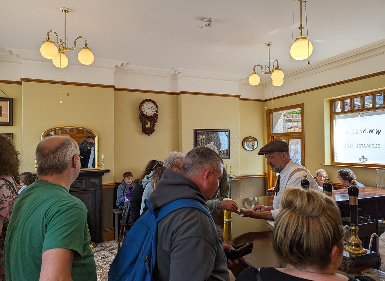 The inside of a pub with a large wooden bar and gold pendant ceiling lights 