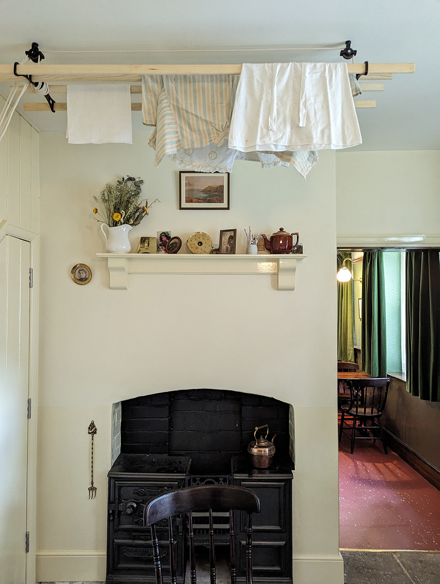 A white room with a small black stove and clothes rail hanging from the ceiling 