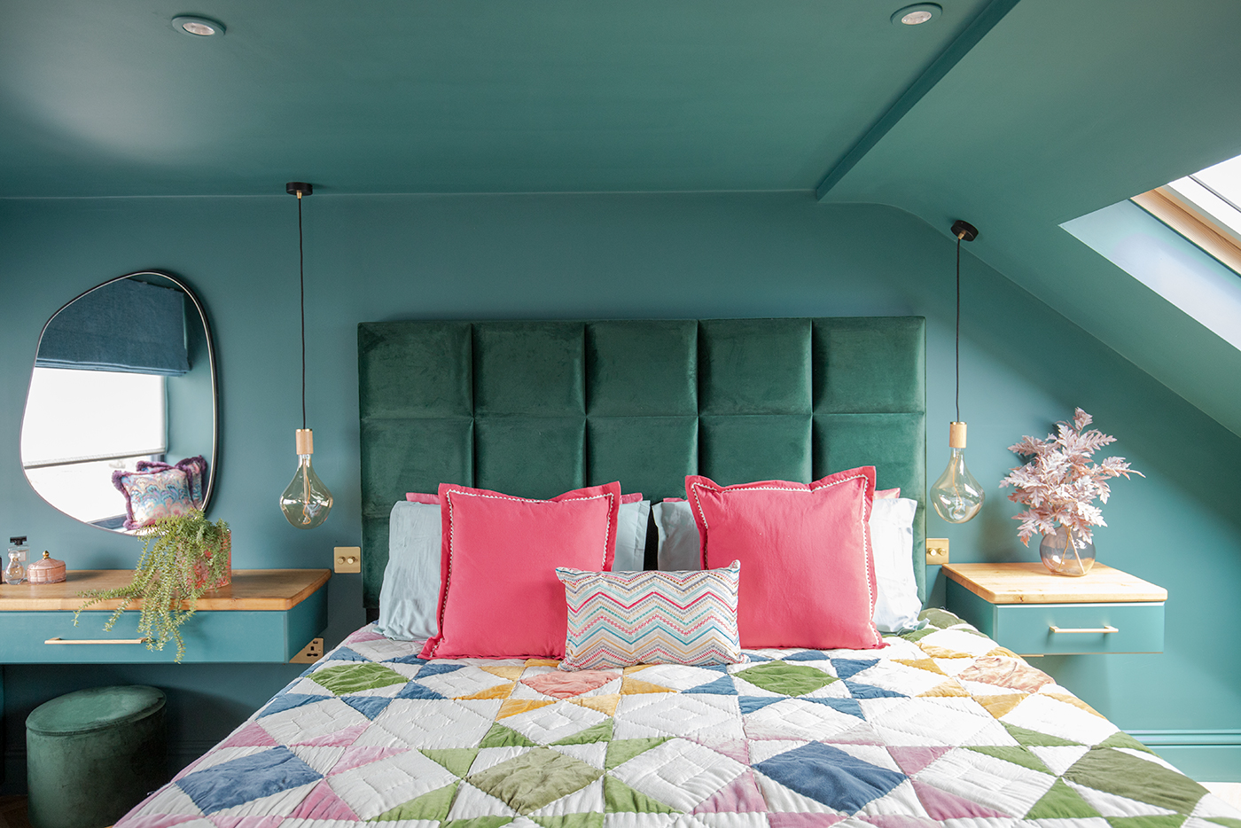 A teal bedroom with a large padded headboard 