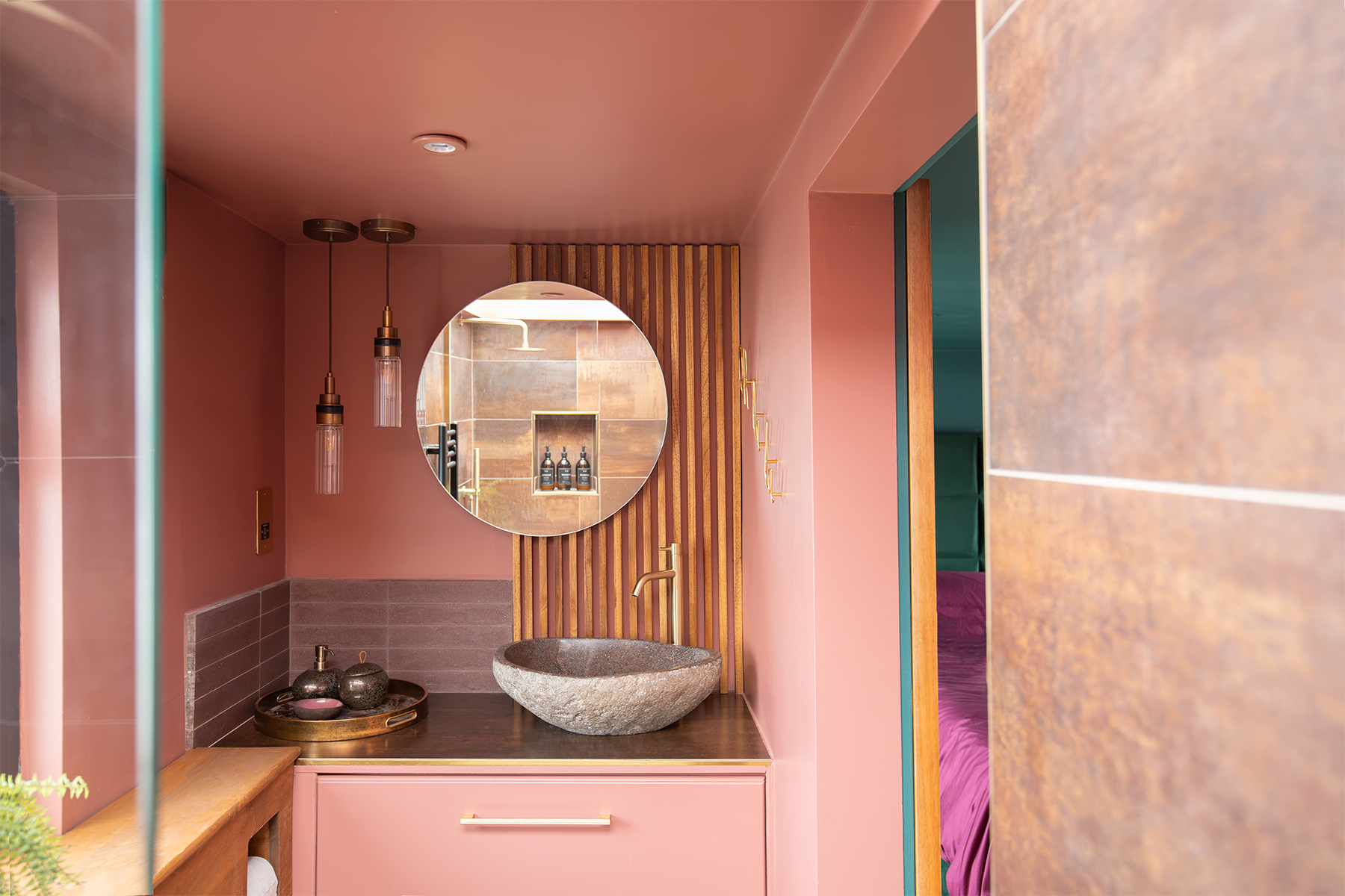 A pink bathroom with a round mirror and stone sink 