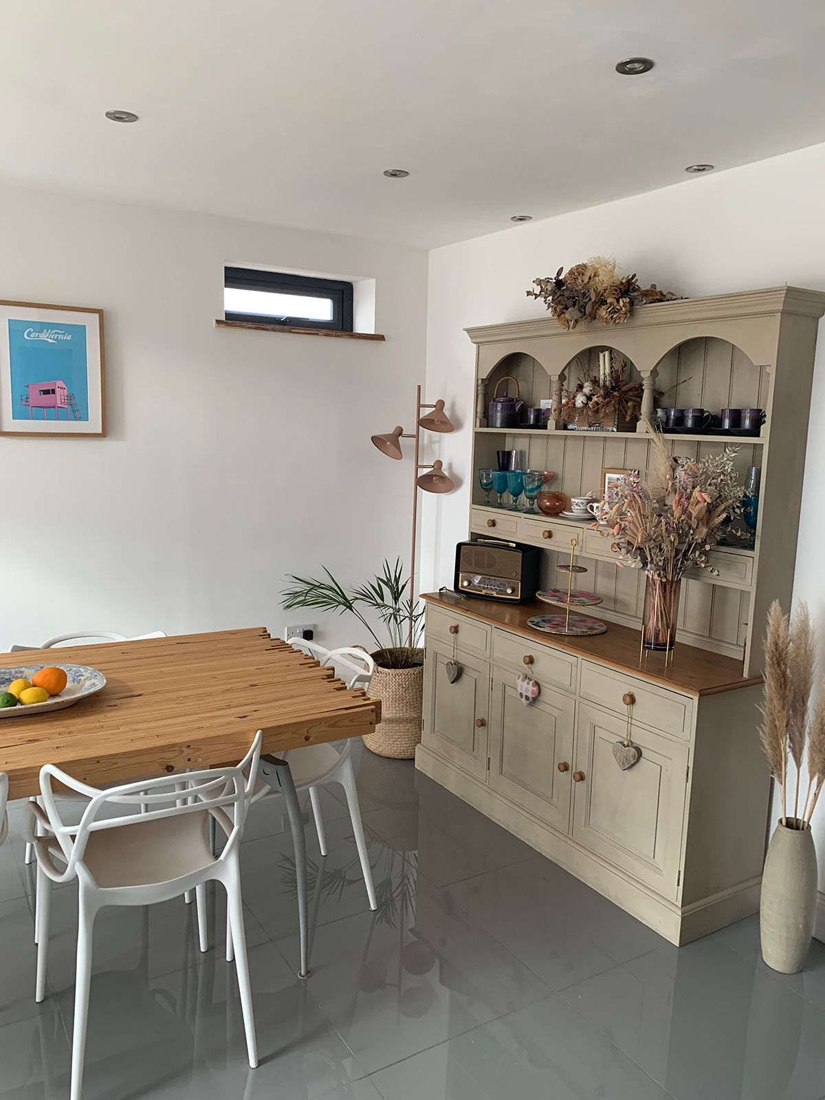 A wooden dining table with white chairs and large wooden welsh dresser 