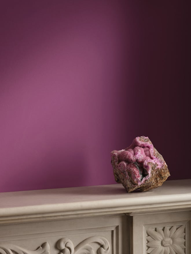 A photo of a wall painted in a rich purple with an amethyst stone in front of it.