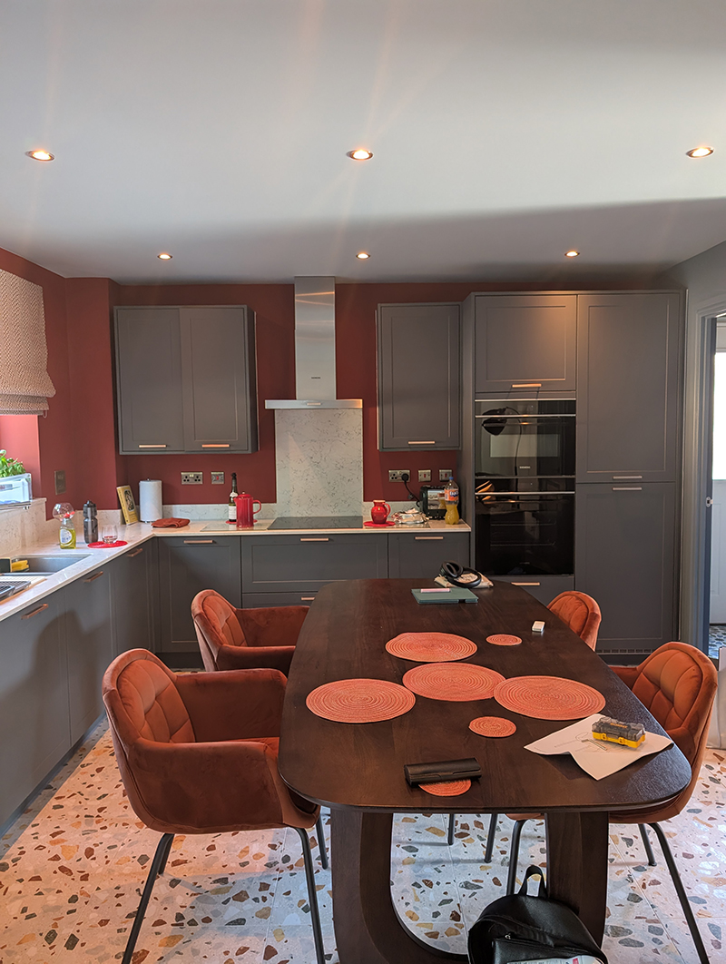 A kitchen with dark wooden dining table and orange velvet chairs 