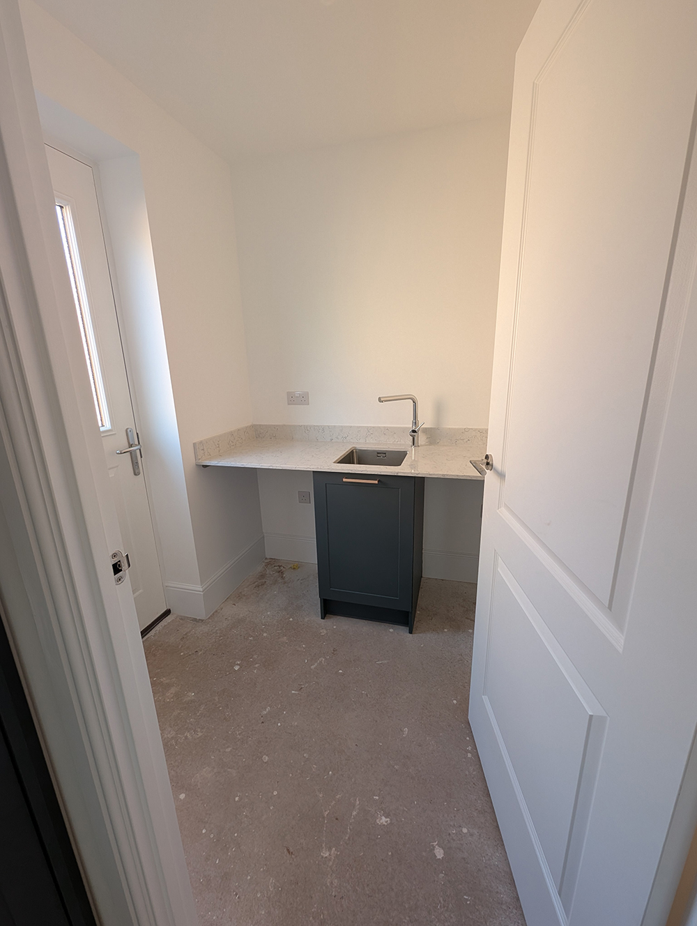A utility room with all white walls and dark green cupboards 