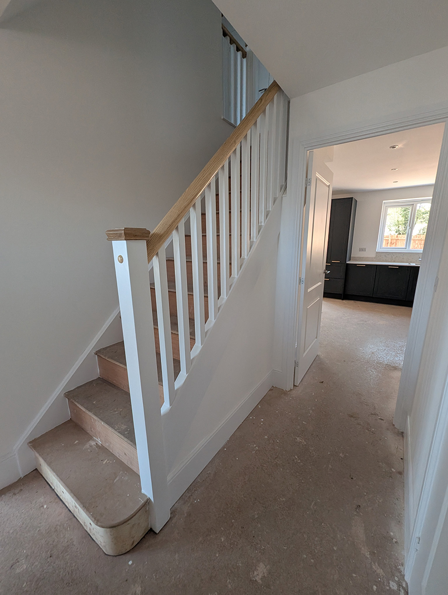A hallway with white walls and a white staircase with no carpet 
