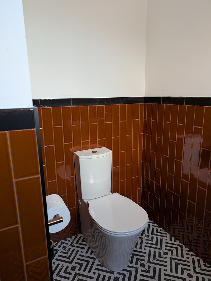 A downstairs toilet with glossy amber tiles half way up the wall 