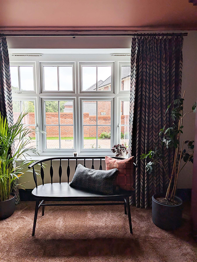 A photo of some colourful curtains in front of a black bench with cushions.