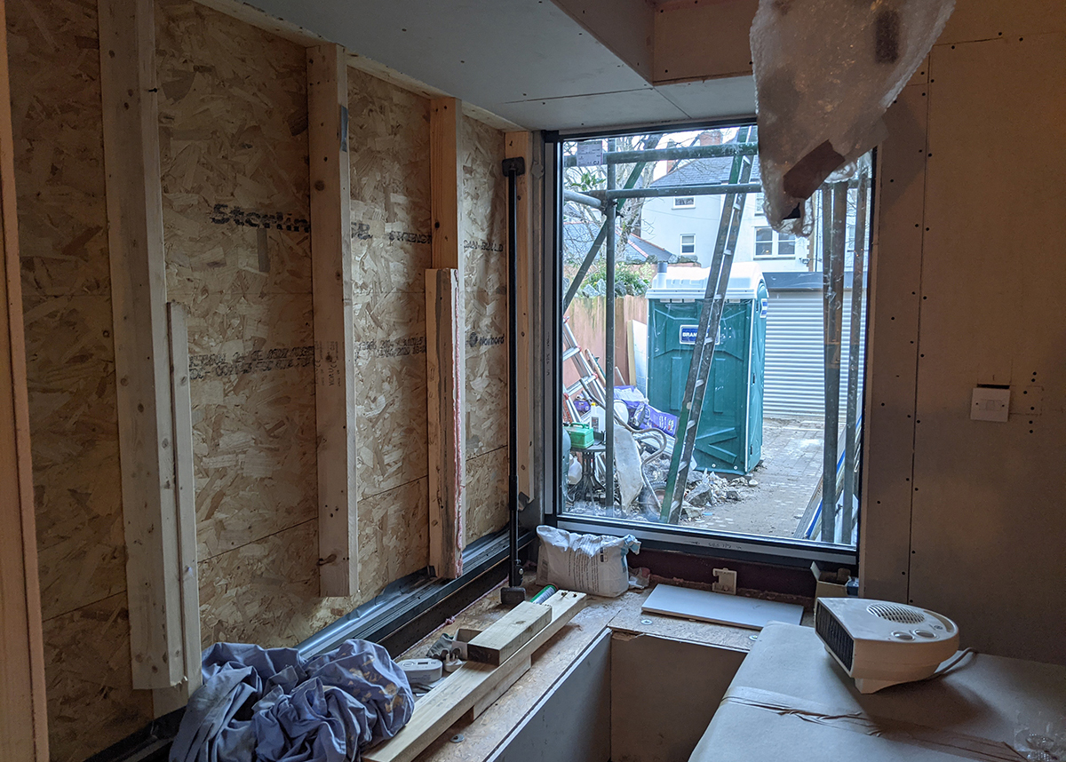 A photo of a corner window area before it is installed - the walls have been opened up and the opening is boarding up.
