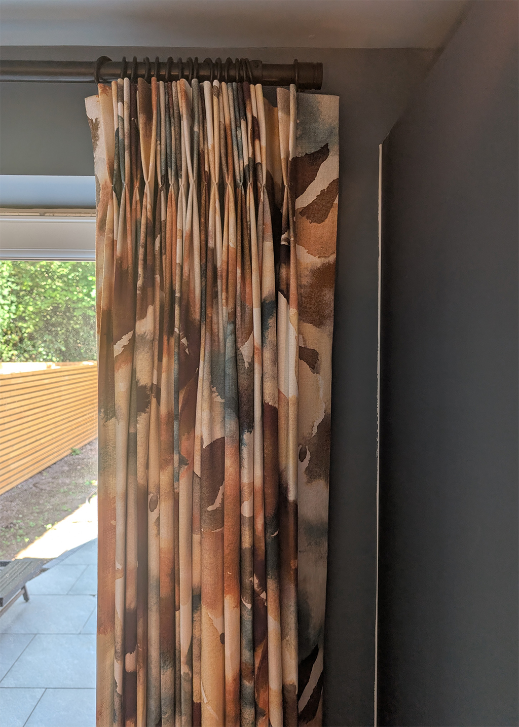 A photo of a double pinch pleat heading curtain on a black metal pole at some French doors.