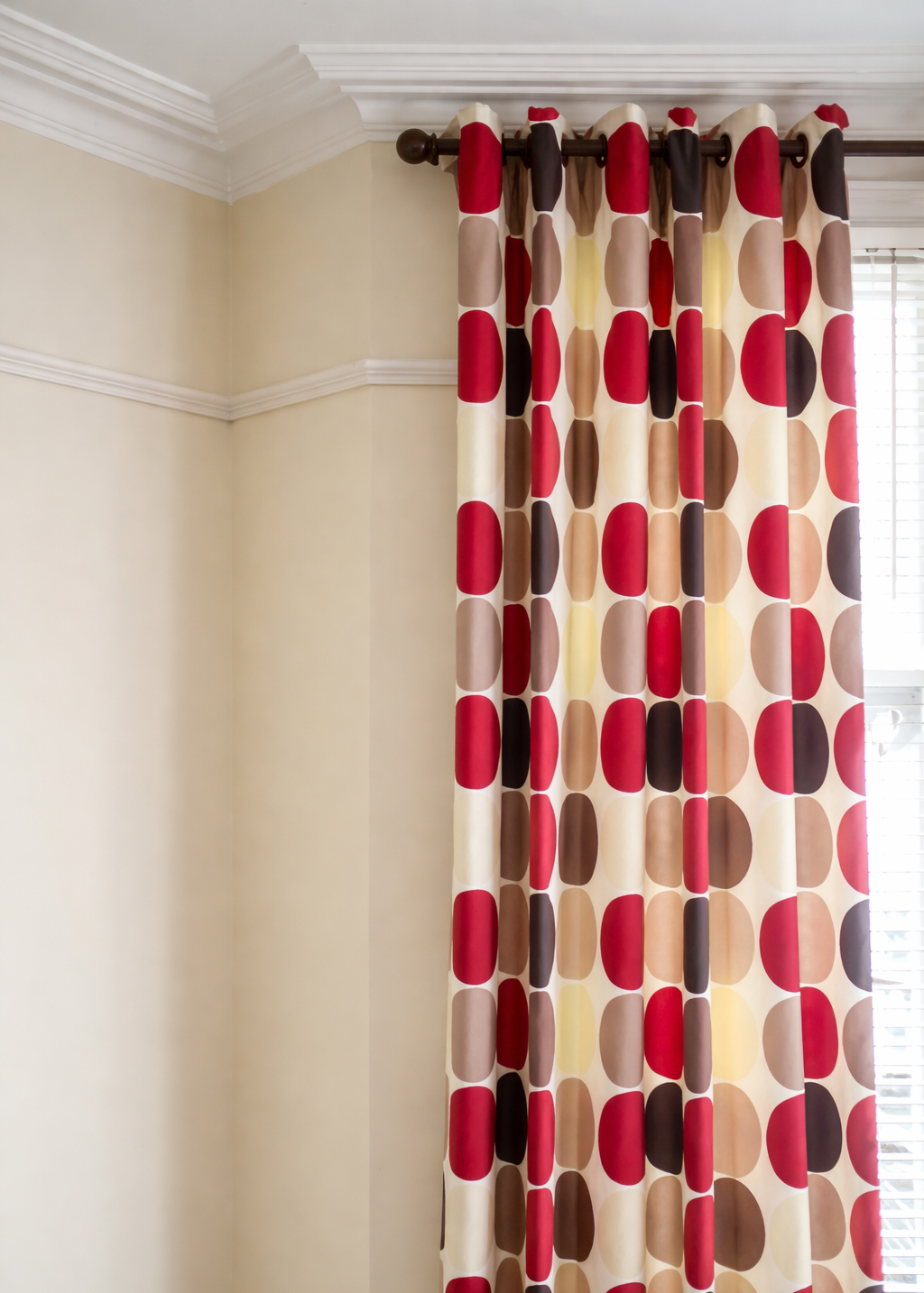 A photo of some eyelet heading curtains on a wooden pole at a window.