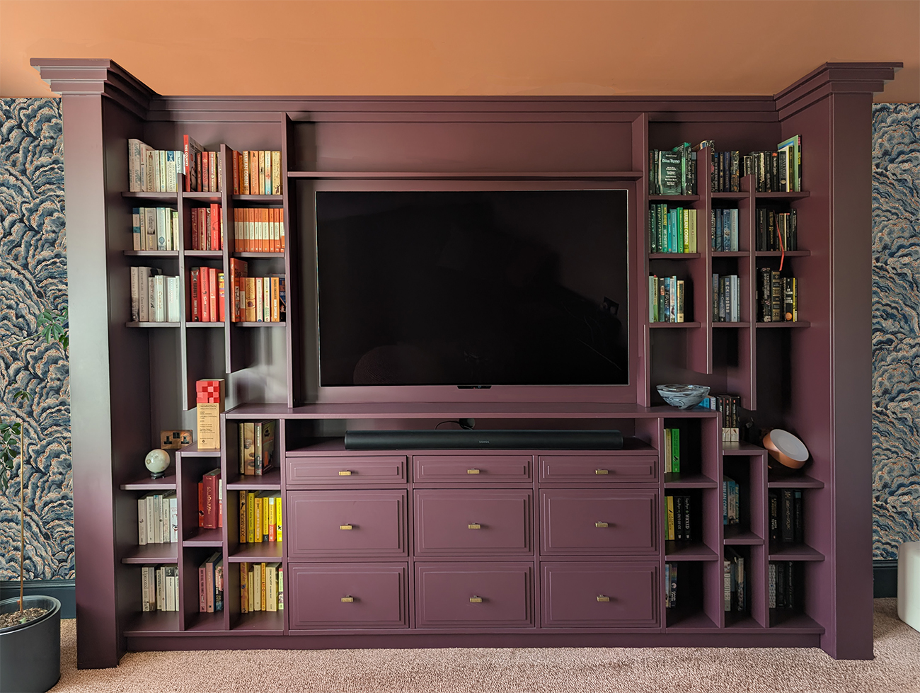 A photo of a 1930s inspired living room media wall painted in an aubergine colour.