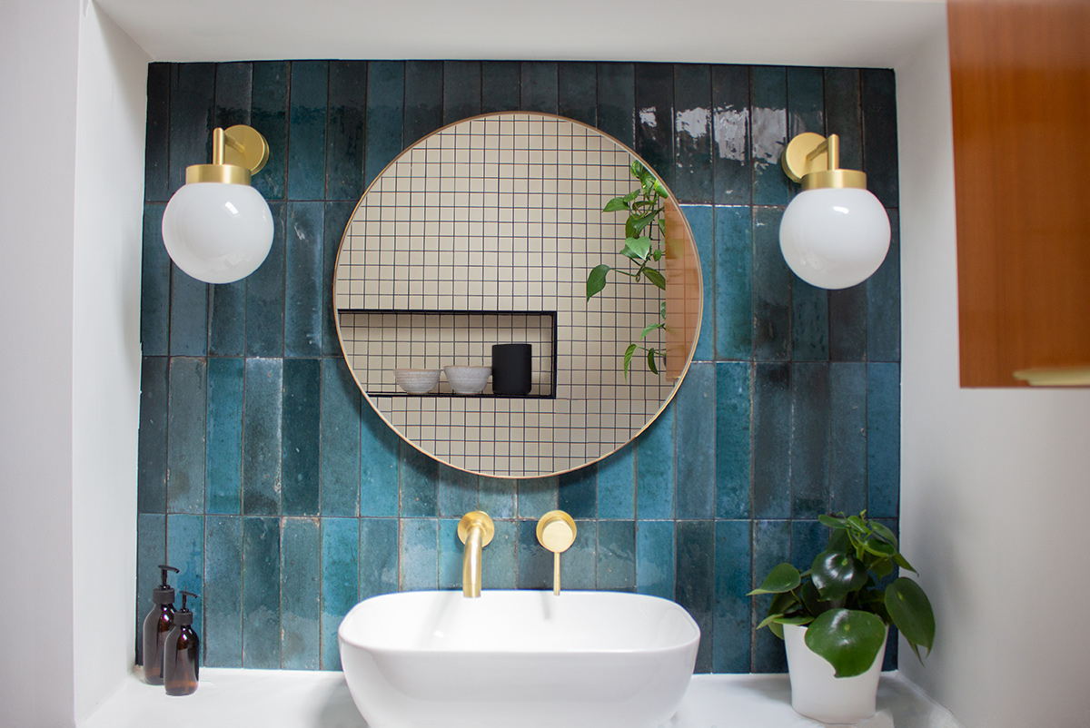A photo of a round mirror over an oval sink with two wall lights on either side of the mirror.