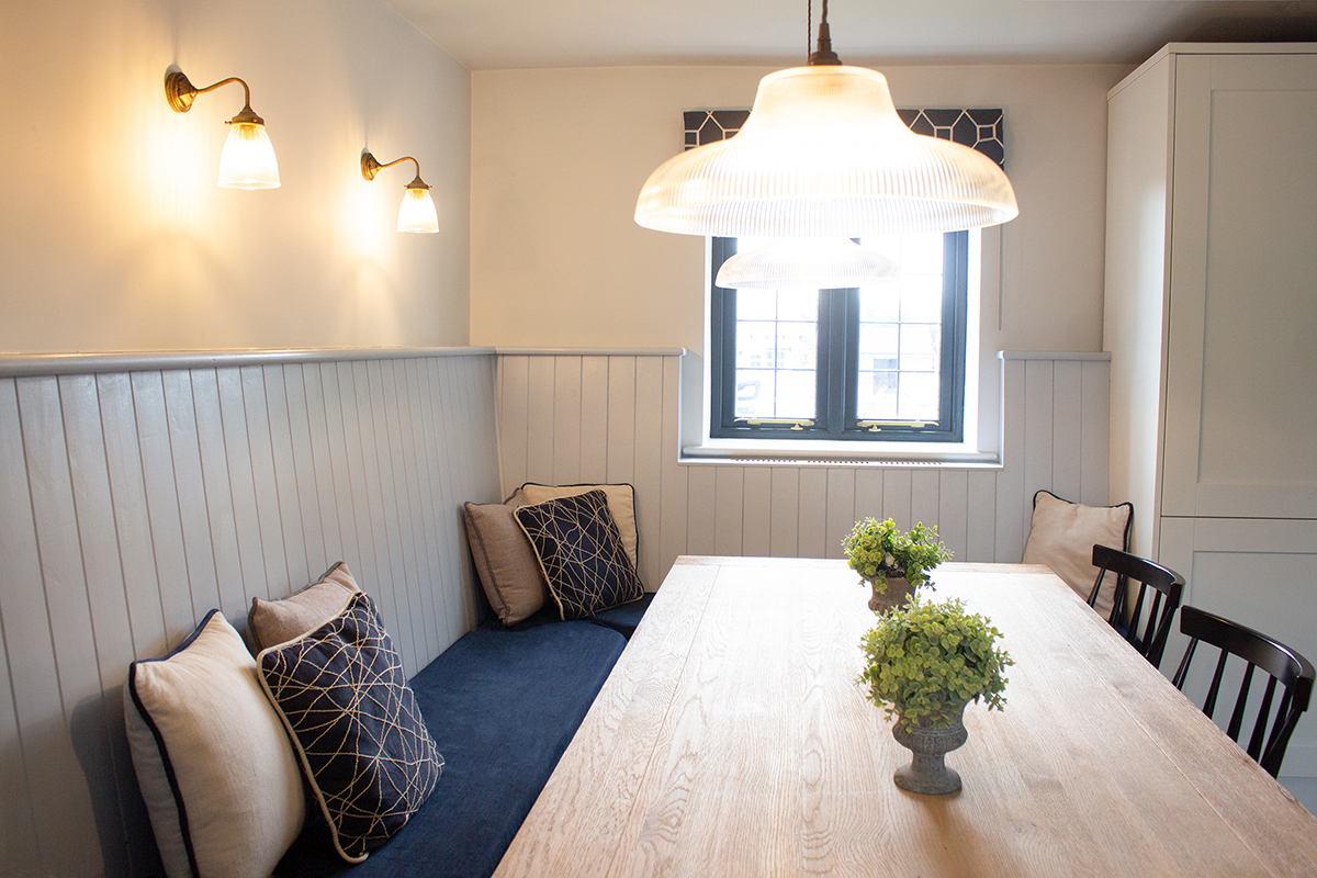 A photo of the other end of the kitchen, showing the softly glowing wall lights and pendant lights over the table.