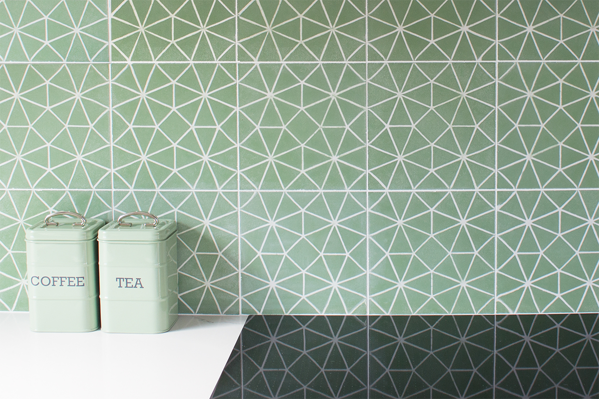 A photo of some sage green patterned tiles on a kitchen splashback, reflected in the black hob.