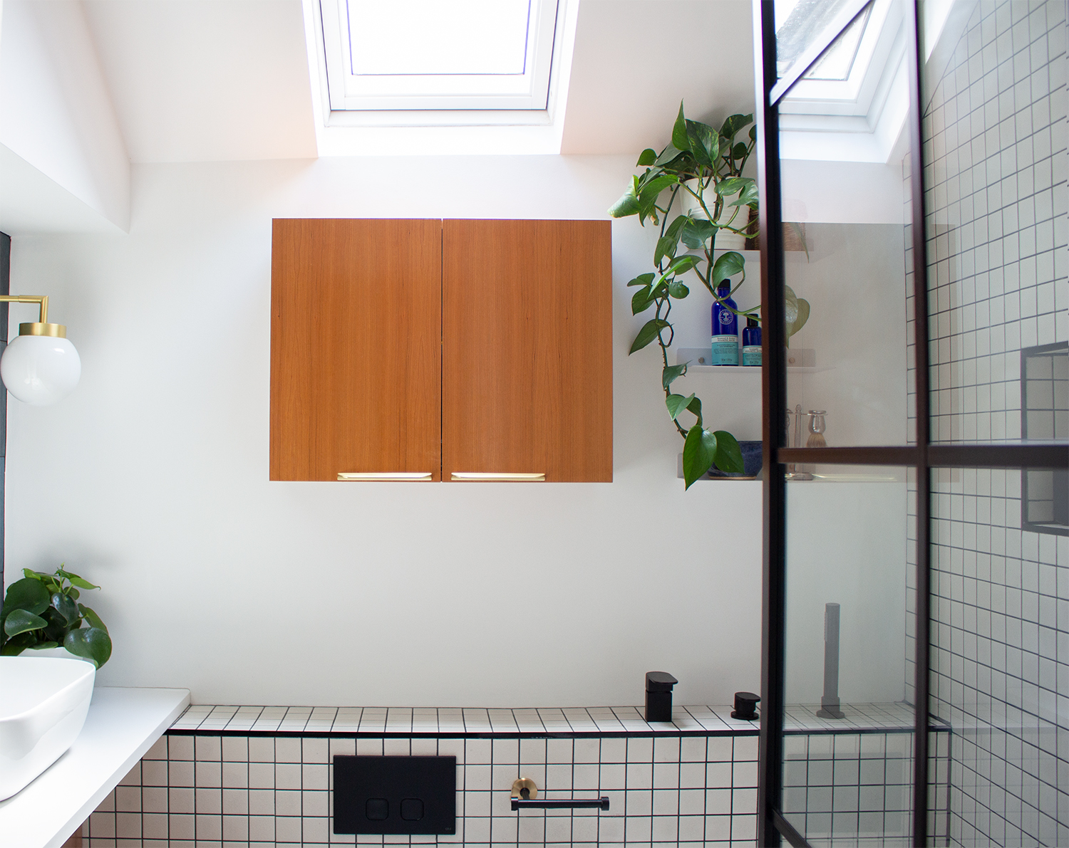 A photo of a white bathroom with off white tiles laid in a grid pattern and a Crittall style shower screen.