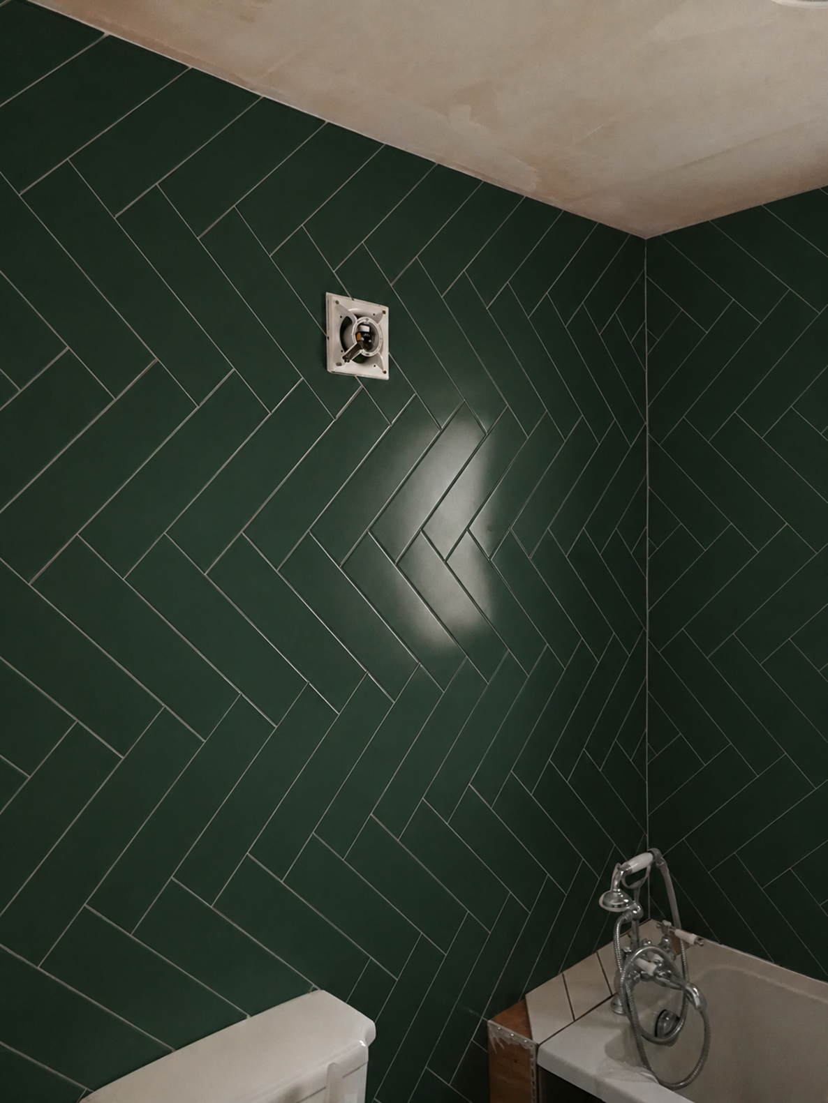 A photo of a smaller bathroom with dark green tiles laid in a herringbone pattern.