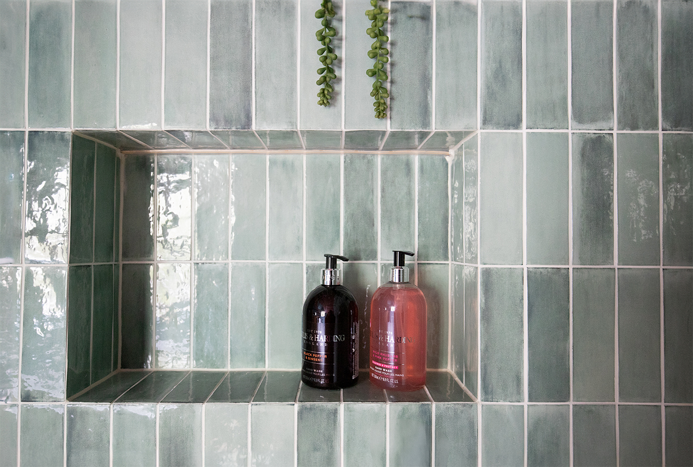A photo of a bathroom with green stacked tiles and a shower niche with mitred tile edges.