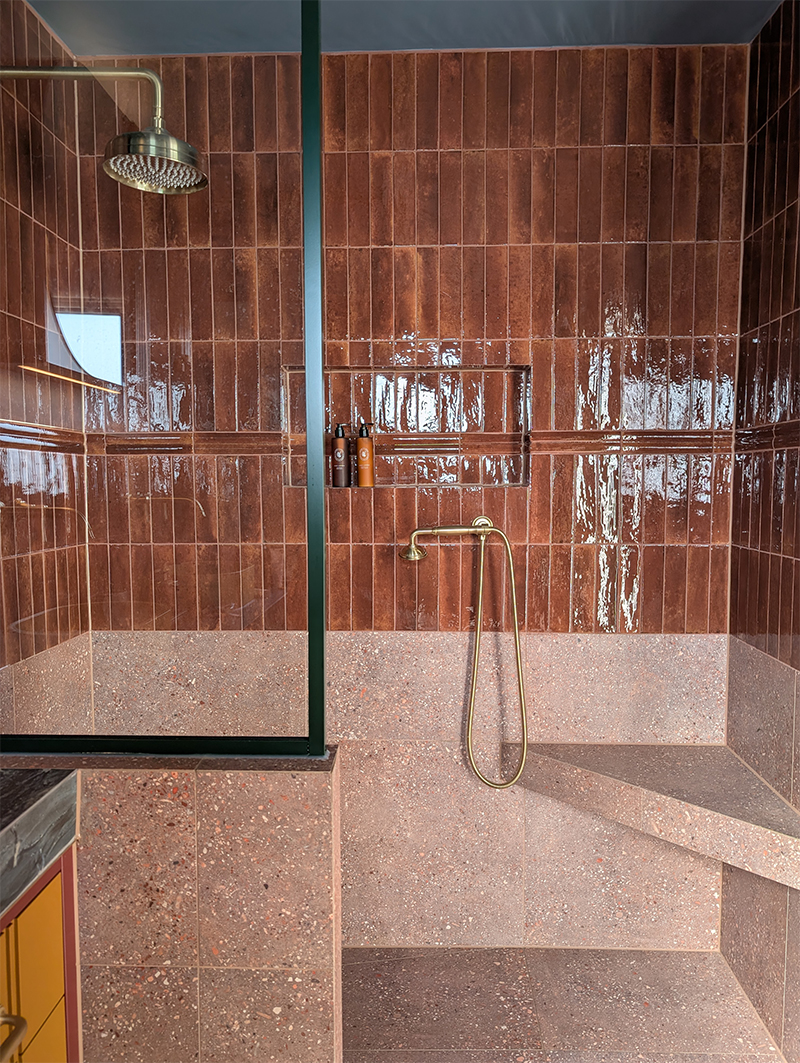 A photo of a wetroom in a bathroom with rust coloured non slip tiles on the floor and halfway up the walls.