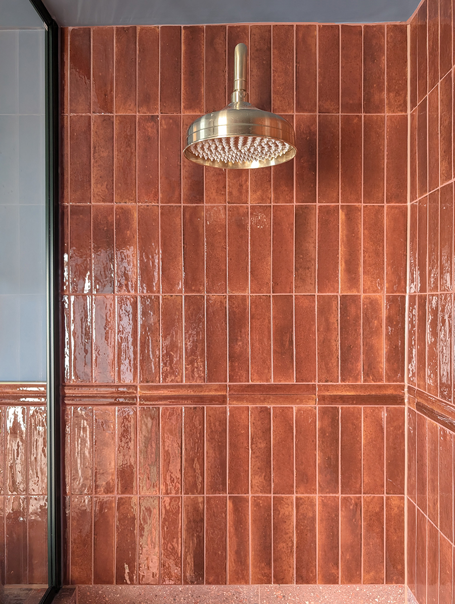 A photo of the same ensuite showing the border tile continung into the shwoer area, with the rust coloured tiles goiung to the ceiling.
