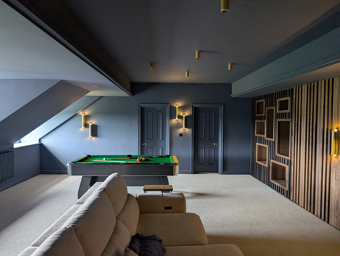 A photo showing the cinema room with the cream sofa in the middle and the pool table behind.