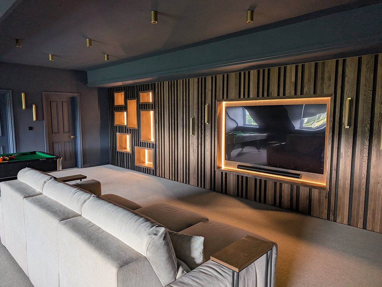 A photo of a cinema room with dark blue walls and a wooden slatted media wall.