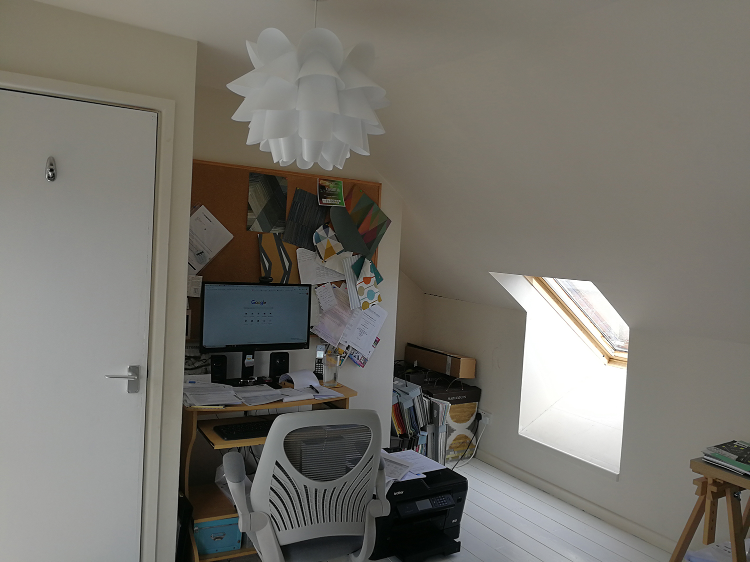 A photo of an office in a loft, with sloping white ceilings and white walls.