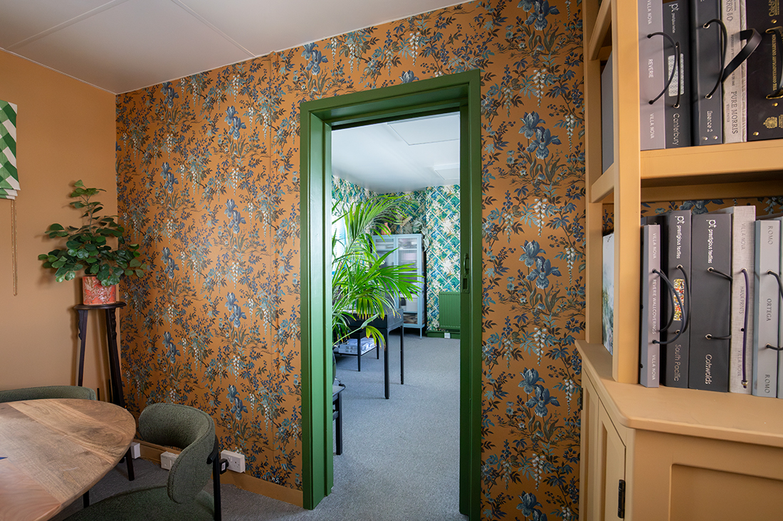 A photo of a small office with mustard yellow walls and wallpaper, with a round desk and chairs in the middle.