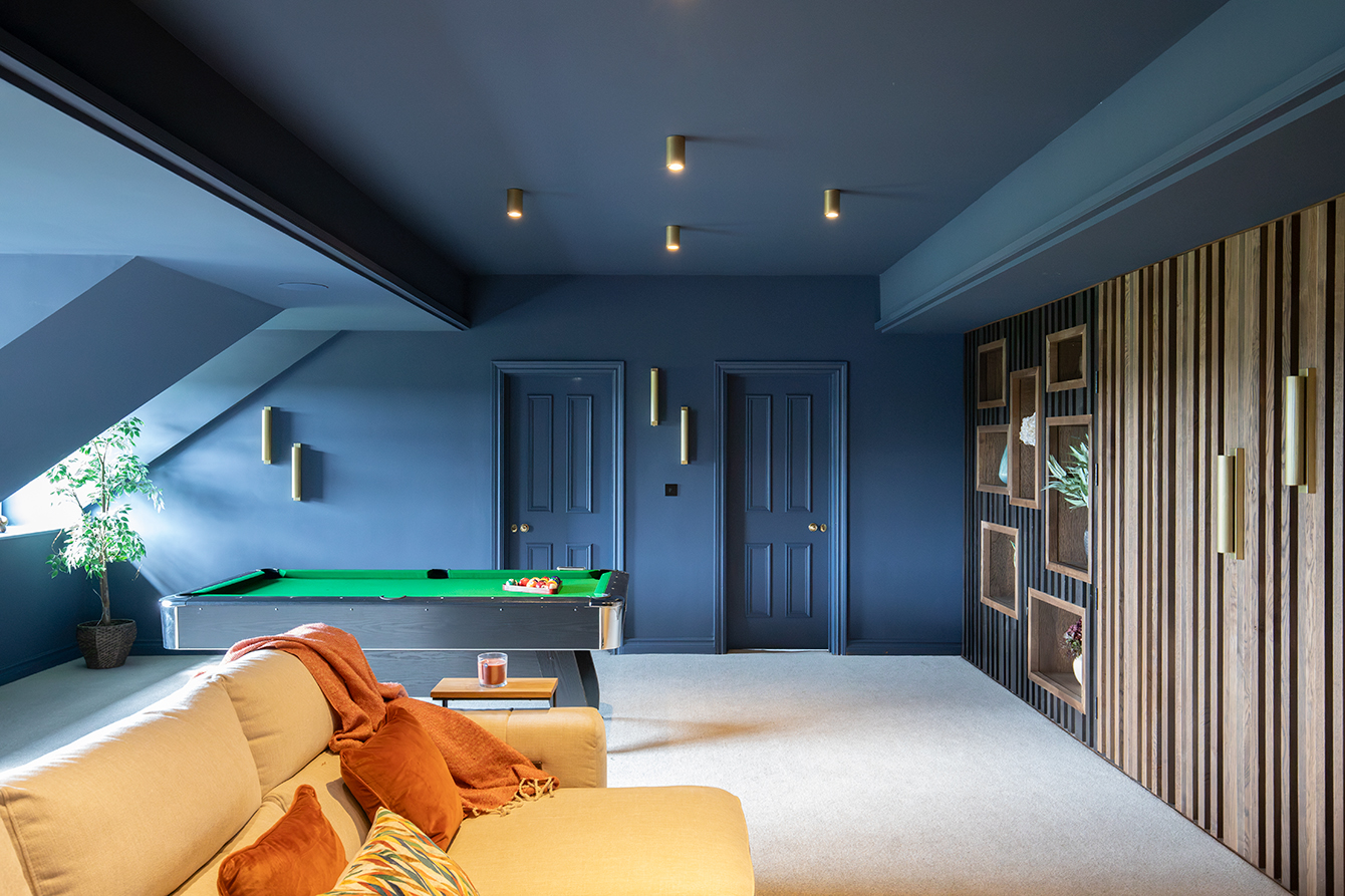 A photo of a dark blue cinema room with a bespoke walnut media wall, with a cut pile cream carpet.