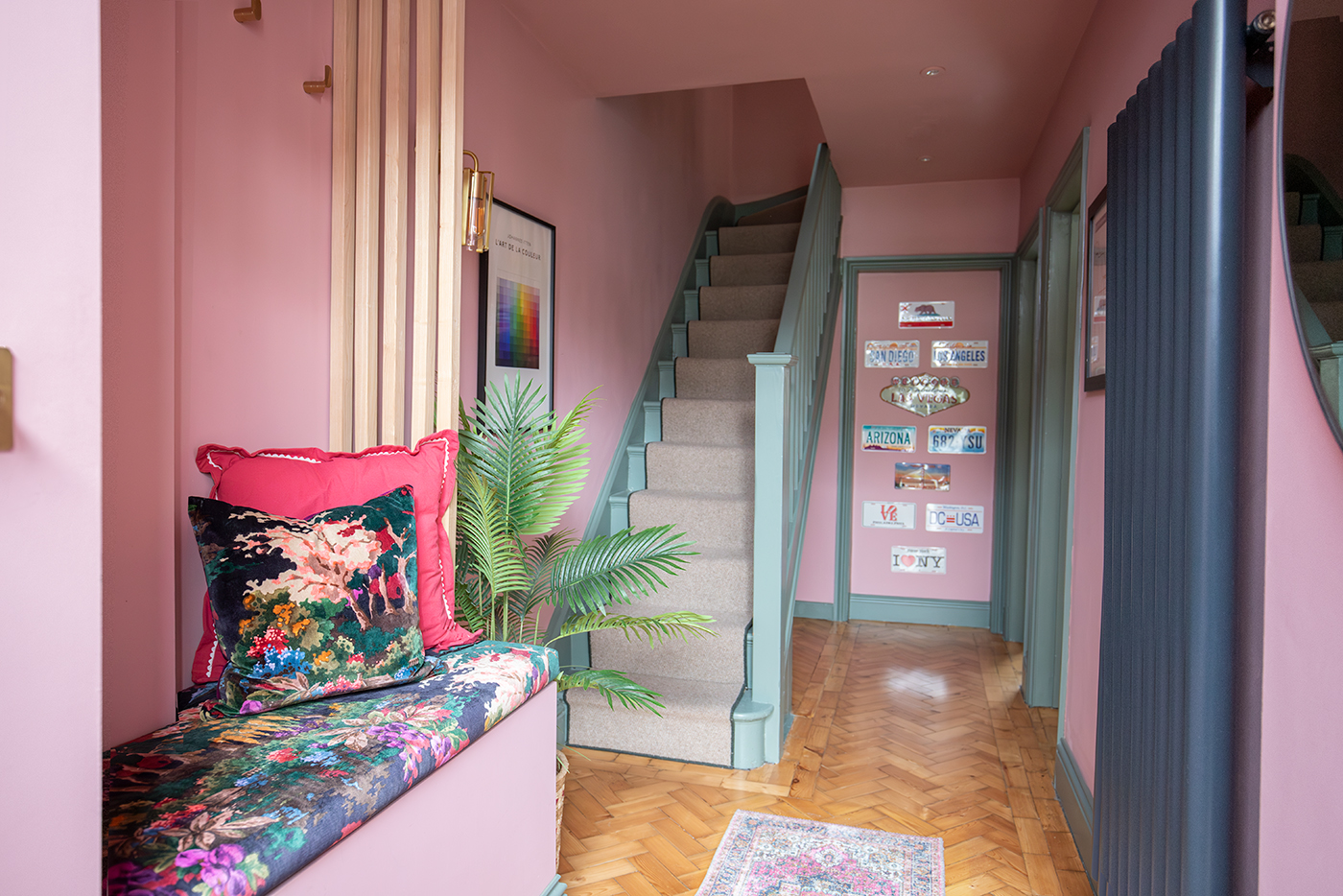A photo of a hallway with pink walls, green woodwork and a flecked runner on the stairs.