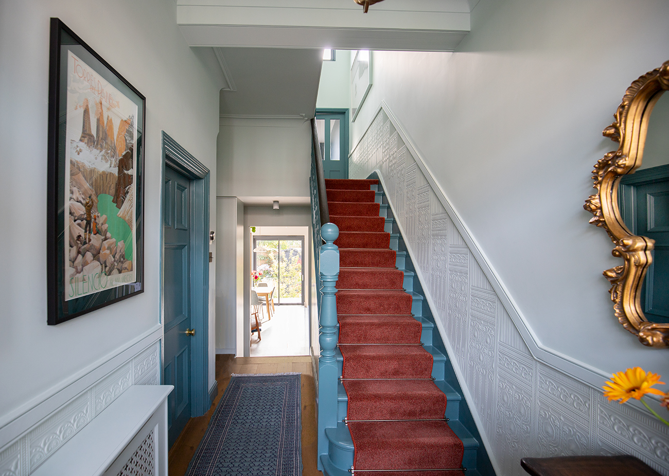 A photo of a hallway with pale blue walls and a rust stair runner carpet.