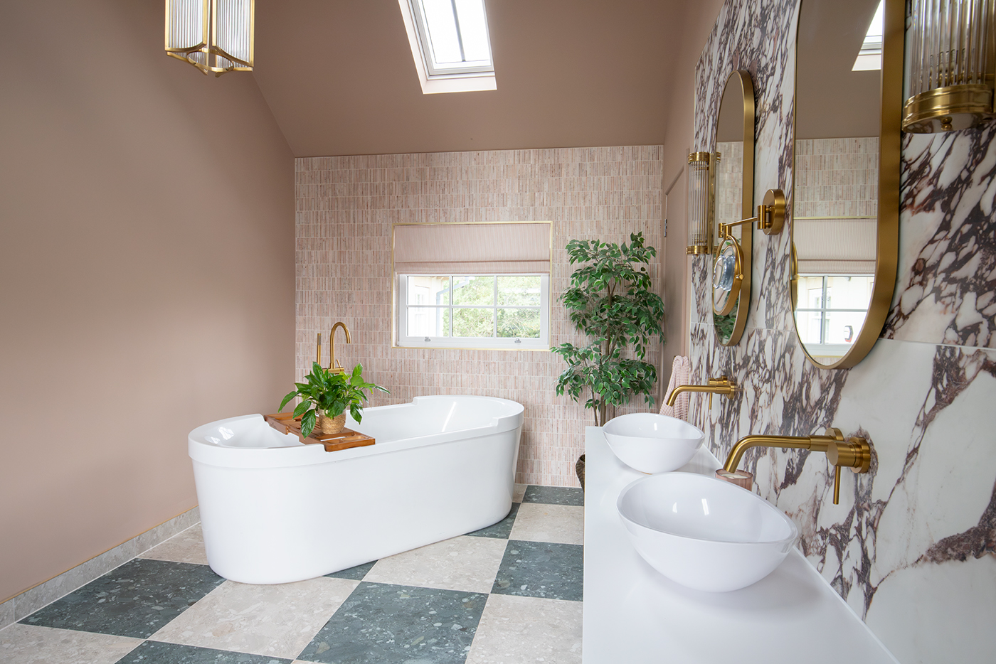 A photo of the en suite shwoing the freestanding bath with a vaulted ceiling above, and dusty pinkk slim tiles on the wall behind the bath.