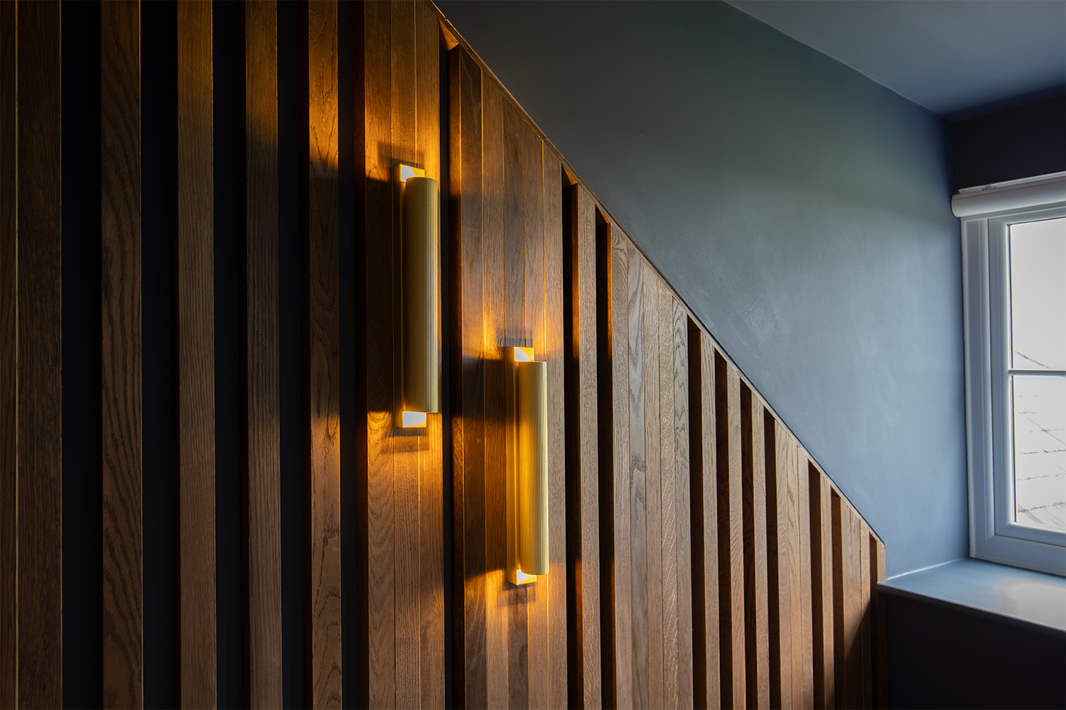 A photo of a pair of the wall lights switched on the slatted wall in the cinema room.