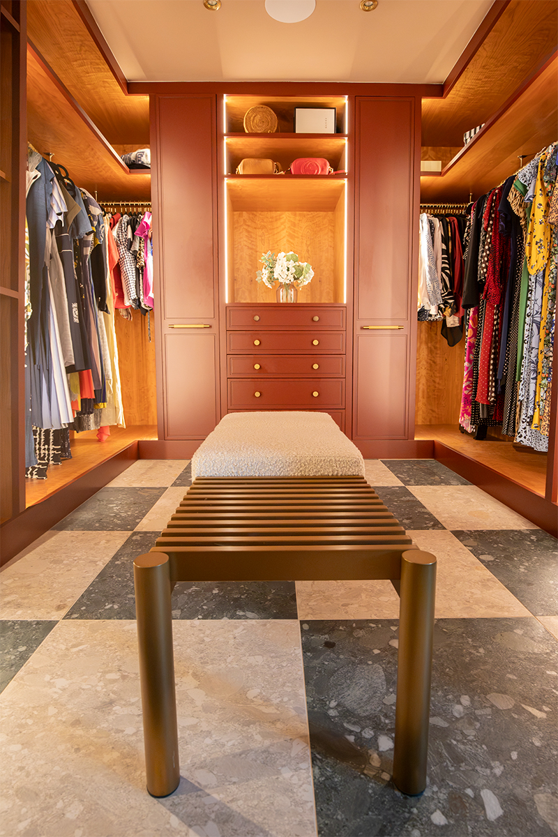 A photo of the dressing room looking along the hanging rails to the drawers at the end. There is a cream boucle bench in the middle of the room.